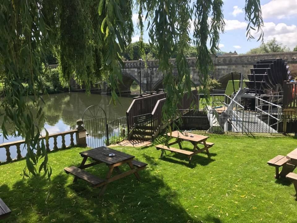 The Old Mill gardens, picnic tables by the Avon under a willow with the bridge and waterwheel behind